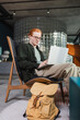 © LIGHTFIELD STUDIOS - Redhead man using laptop near suitcase in hotel lobby