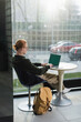 © LIGHTFIELD STUDIOS - Redhead freelancer using laptop with chroma key near backpack in hotel lobby