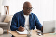 Black Man Using Laptop Taking Notes In Office, Wearing Eyeglasses
