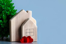 Two Wooden Houses On Blue Background With Green Plant And Two Red Hearts. Concept Of Love In House, Romance In Family, Sale Of Houses. Invitation To Housewarming, Wedding. Postcard For Your Beloved.