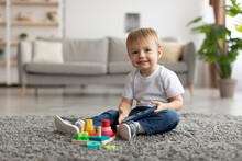 Happy Little Toddler Boy Watching Cartoon On Smartphone While Sitting On Floor Carpet, Looking And Smiling At Camera