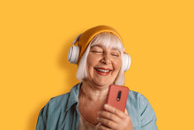 Happy 50s Caucasian Woman Headphones Listen To Music Sing Song Record Voice By Mobile Cell Phone Dictaphone On Yellow Color Background Studio Portrait.
