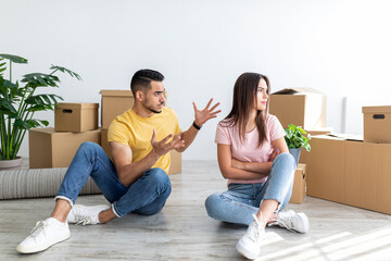 Poster - Unhappy young multiracial couple having argument, sitting on floor in their new apartment on moving day