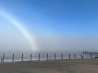 Wall Mural - Beautiful beach landscape tranquil scene with fogbow over sandy shore by ocean at Happisburgh in Norfolk coast in East Anglia uk with blue skies after foggy mist cold morning in December