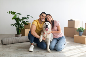 Wall Mural - Cheery young international couple with cute golden retriever dog sitting on floor of new home on relocation day