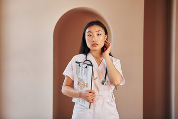 Wall Mural - Documents in hands. Young serious asian woman standing indoors