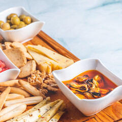 Bowls with picked mussels and olives on a cheese board and breadsticks on a white table. Appetizer.