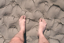 Man's Barefooted Feet Walk On Dry Cracked Sand By The River Coast. Summer Walking In Wild Place On Nature. Adventure, Resting Outdoors, Global Warming Concept.