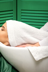 Wall Mural - Hairdresser wraps hair of a young caucasian woman in a white towel after washing head in the hairdressing salon