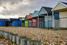 A Row Of Colorful Beach Huts On A Stony English Beach. Empty Beach Huts On A Cold Overcast Day.