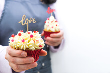 Woman Waitress With Two Cupcakes Decorated With Red Hearts Topping And Wooden Sign With LOVE Letters. Valentine's Day. White Background.