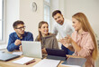 © Studio Romantic - Group of happy smart university students sitting at desk in classroom, working on project together, using laptop and tablet, discussing business startup ideas, doing Internet research on the subject
