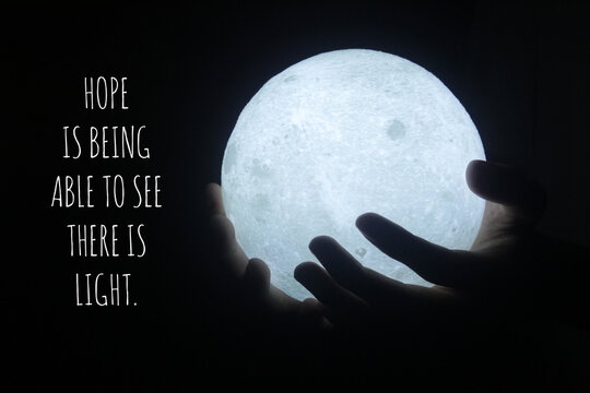Wall Mural -  - Hope inspirational motivational quote - Hope being able to see there is light. With person holding light of moon lamp in hand on dark black background. Hope and faith concept.