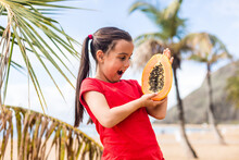 Portrait Of A Cute Little Girl With Papaya Against A Background Of Palm Trees