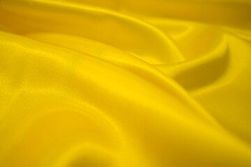 Abstract Gold Satin Silky Cloth Fabric Textile Drape with Crease Wavy Folds background.With soft waves and,waving in the wind Texture of crumpled paper. Background texture, pattern. Yellow silk fabric