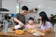 © Shisu_ka - Asian family breakfast at home. Parents and children enjoy eating together, talking with laughter and good atmosphere. Father and mother plays with son playfully at kitchen table.