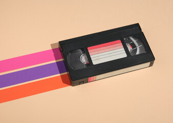 VHS video cassette on pastel background with colored stripes. Minimalistic retro composition.