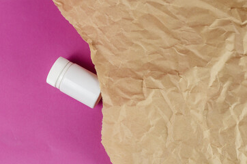 White plastic vial and Crumpled wrapping paper against a magenta