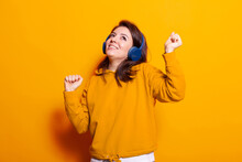 Playful Person Dancing And Listening To Music On Headset In Studio. Positive Woman Feeling Relaxed And Doing Dance Moves While Using Headphones To Enjoy Sounds And Song Over Orange Background