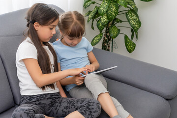 Two little sisters using tablet at home. Watching something funny.