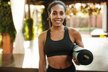 Wall Mural - Black woman smiling at camera while standing with yoga mat