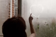 A woman draws heart with her finger on a wet fogged window. The concept of romance, falling in love.