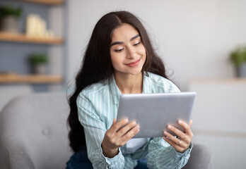 Wall Mural - Charming Indian lady using tablet computer, studying remotely or having online conference at home