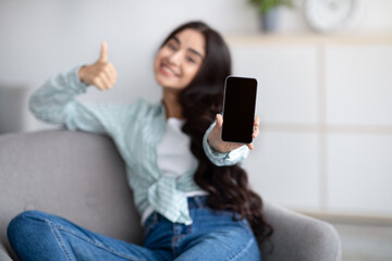 New mobile app mockup. Charming Indian woman showing cellphone with empty screen, gesturing thumb up at home