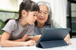 © Prot - Asian Grandmother with her two grandchildren having fun and playing education games online with a digital tablet at home in the living room. Concept of online education and caring from parents.