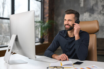 Wall Mural - Office employees concept. Focused caucasian man wearing wireless headset is using laptop for online video conversation, talking with customers or coworkers online