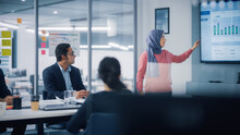 Multi-Ethnic Office Conference Room. Brilliant Muslim Female CEO Wearing Hijab Does Presentation For Group Of Managers Talking, Using TV Infographics, Statistics. Innovative Businesspeople.