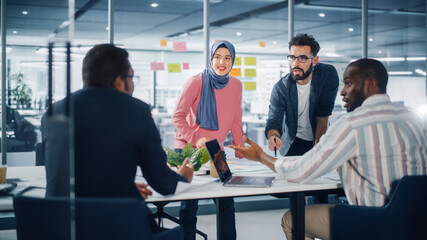 Diverse Modern Office: Muslim Businesswoman Wearing Hijab and Stylish Hispanic Entrepreneur Lead Business Meeting, Use Laptop, Talk, Brainstorm with Managers. Young Professionals on e-Commerce Project