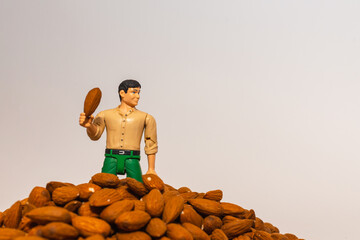 Miniature toy man farmer holds almond on a pile of almond nuts.white background.Health concept.Copy space.