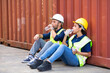 © NVB Stocker - Tired hispanic male and female container worker in hardhat and uniform resting at container yard port of import and export.