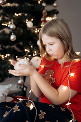 Wall Mural - A teenage girl in a red festive T-shirt sitting with a hamster in her hands at the Christmas tree