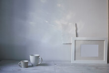 Scandinavian Style. Interior Design. A White Cups Of Different Size, A Frame For A Photo Are On The Table. The Blank Sheets Of Paper Are Attached To The Wall. Empty Space For Text