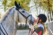 Beautiful girl rider in uniform, kisses with the lips of a horse