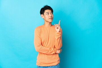 Wall Mural - Young Chinese man isolated on blue background pointing up a great idea