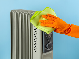 Hand wiping the oil filled electric heater with microfiber cloth. Сleaning the space heater from dust. Household chores, cleaning and maintenance of domestic appliances concepts.