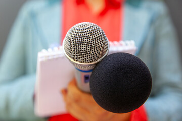 Microphone in the focus, blurred female journalist at news conference or media event taking notes