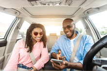 Happy Black Couple Driving Car And Using Cell Phone