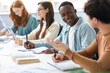 © Prostock-studio - Diverse group of students sitting at desk writing and talking