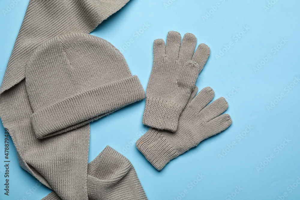 Warm gloves, hat and scarf on color background