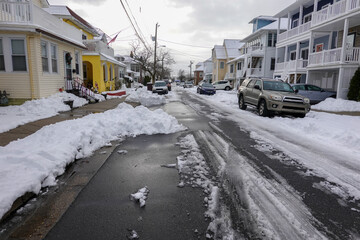 Small one way snow covered street with the center partially plowed and cars parked on both sides in deep snow