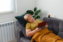 Elderly Female Browsing Tablet On Couch