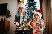 Siblings Making Weird Faces In Front The Christmas Tree