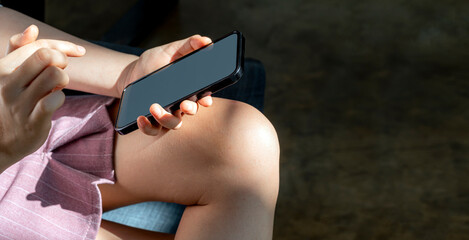 Wall Mural - young woman using smartphone while sitting at home, under the sunlight from window.