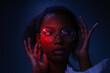 © Anna Berkut/Stocksy - female studio portrait in neon light, wearing glasses