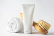 SPA cosmetics, woman body and skincare products on white background. Natural bristle dry massage brush and body or face cream in white plastic tube.