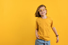 Joyful Little Kid Girl 8-10 Years Old In Yellow T-shirt And Eyeglasses On Daffodil Color Trend Wall Background Studio Portrait. Gender Neutral Child Having Fun. Childhood Lifestyle Concept.